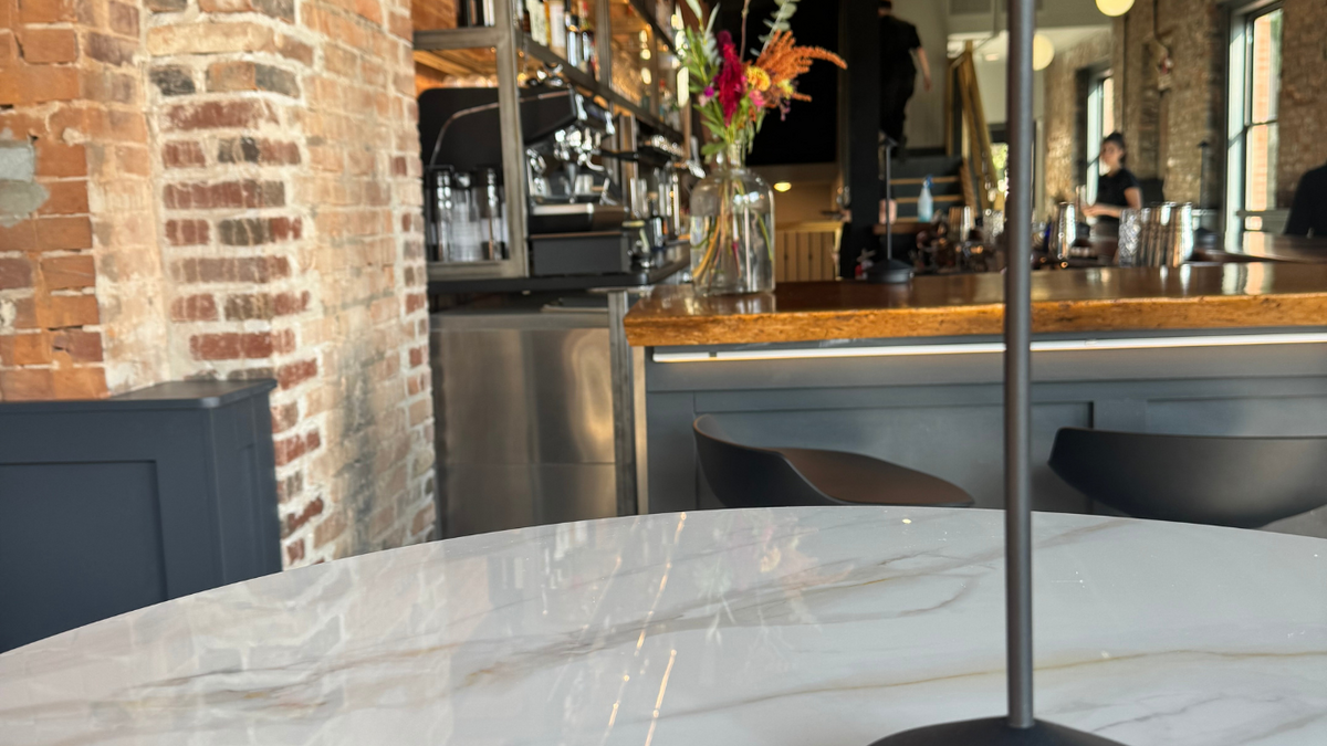 a round, white-marble dining table with black lamp sitting on it and a cocktail bar in the background
